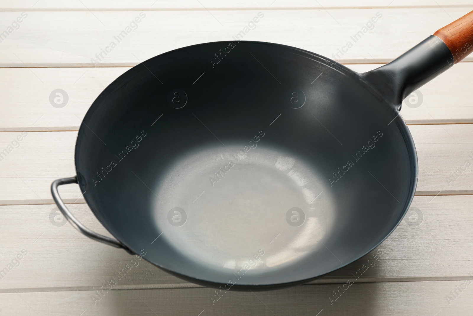 Photo of Empty iron wok on white wooden table. Chinese cookware