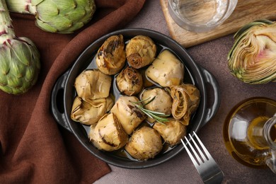 Photo of Delicious pickled artichokes with rosemary served on brown table, flat lay