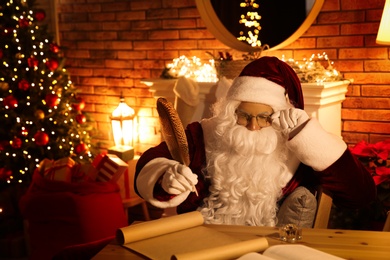 Photo of Santa Claus with wish list at table indoors