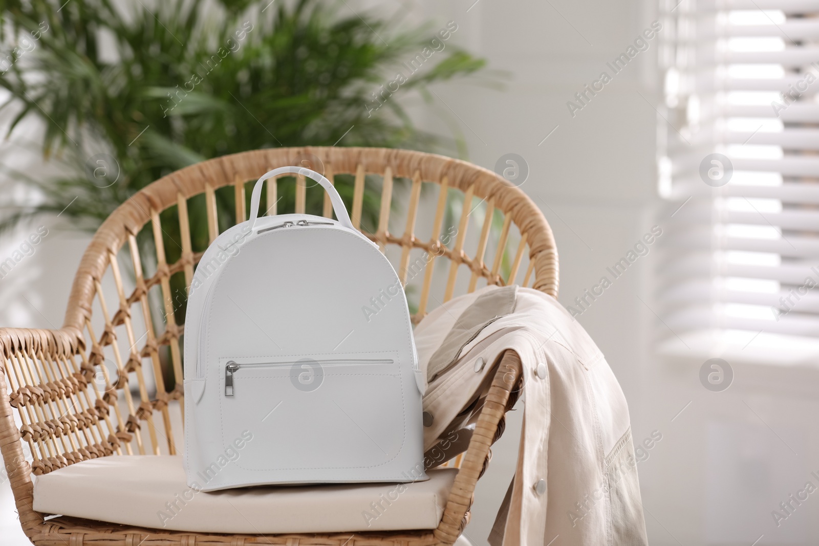 Photo of Stylish white backpack and jacket on wicker chair indoors