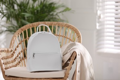 Photo of Stylish white backpack and jacket on wicker chair indoors