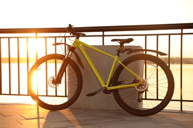 Photo of Yellow bicycle parked near railing on city waterfront at sunset