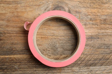 Photo of Roll of pink adhesive tape on wooden background, top view