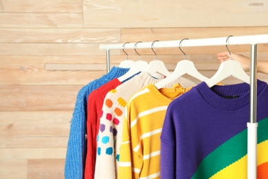 Photo of Collection of warm sweaters hanging on rack against wooden background