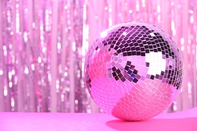 Photo of Shiny disco ball on blurred background, toned in pink. Space for text