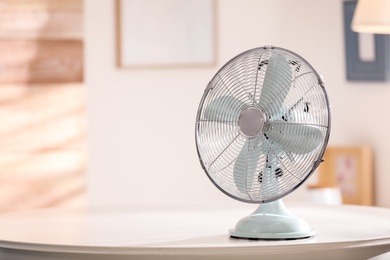 Photo of Modern electric fan on white table indoors. Space for text