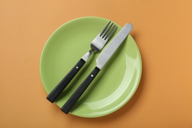 Green ceramic plate with cutlery on pale orange background, top view