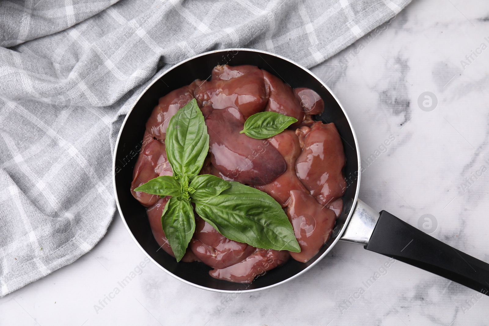 Photo of Raw chicken liver with basil in frying pan on white marble table, top view