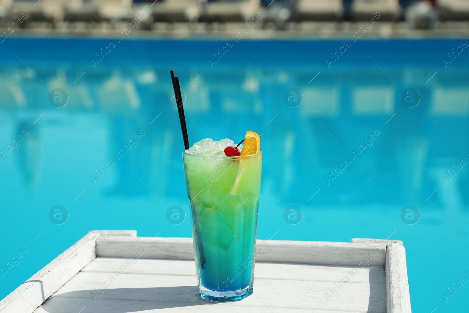 Photo of Refreshing cocktail on wooden table near swimming pool outdoors