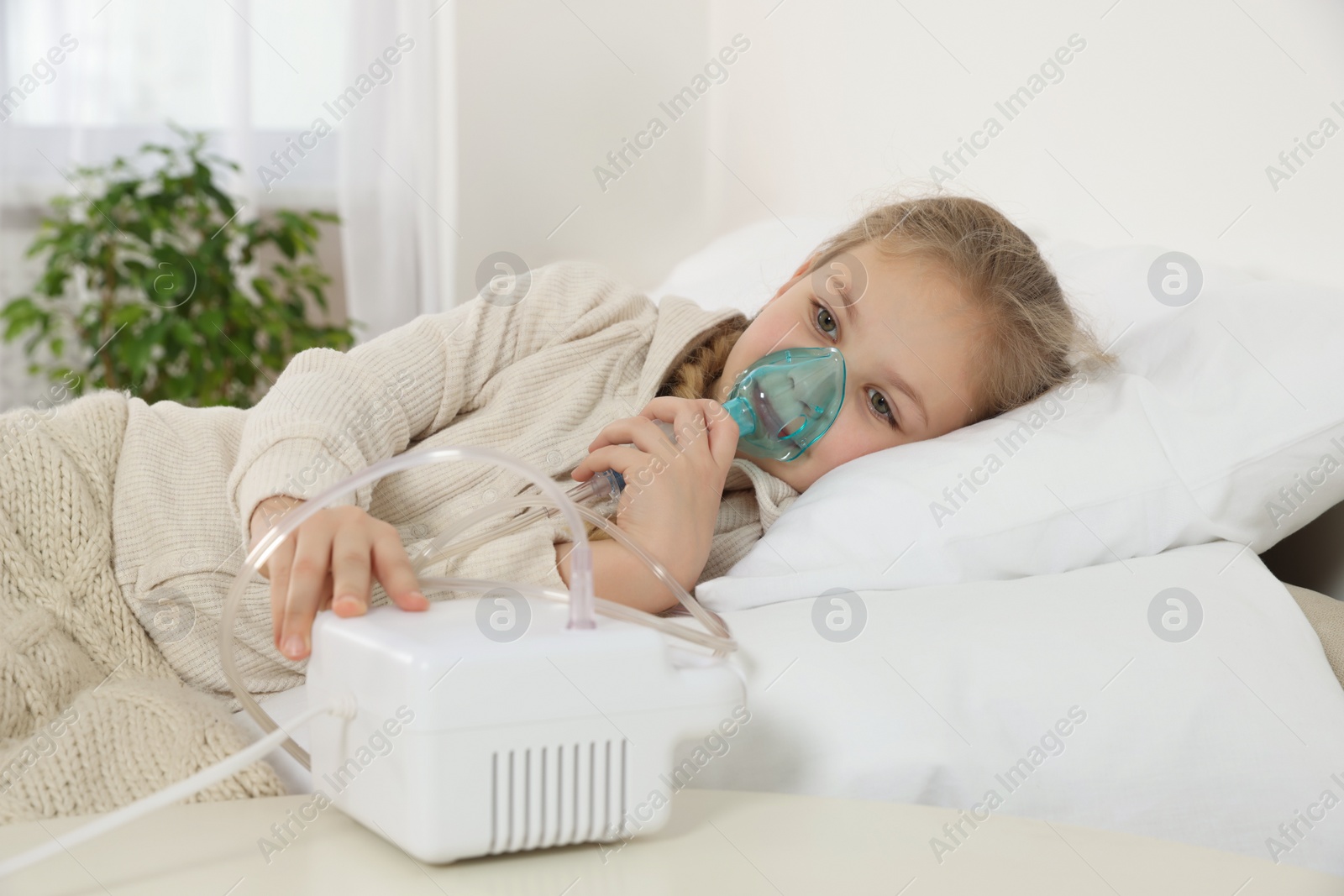 Photo of Little girl using nebulizer for inhalation on bed at home