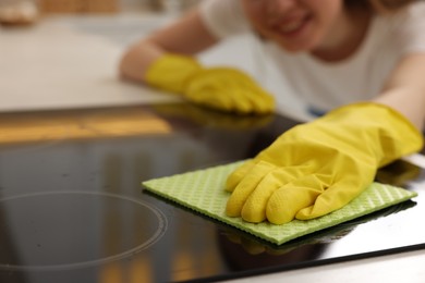 Photo of Woman with spray bottle and microfiber cloth cleaning electric stove in kitchen, closeup