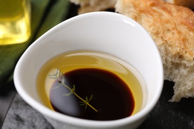 Photo of Bowl of organic balsamic vinegar with oil, thyme and bread on table, closeup