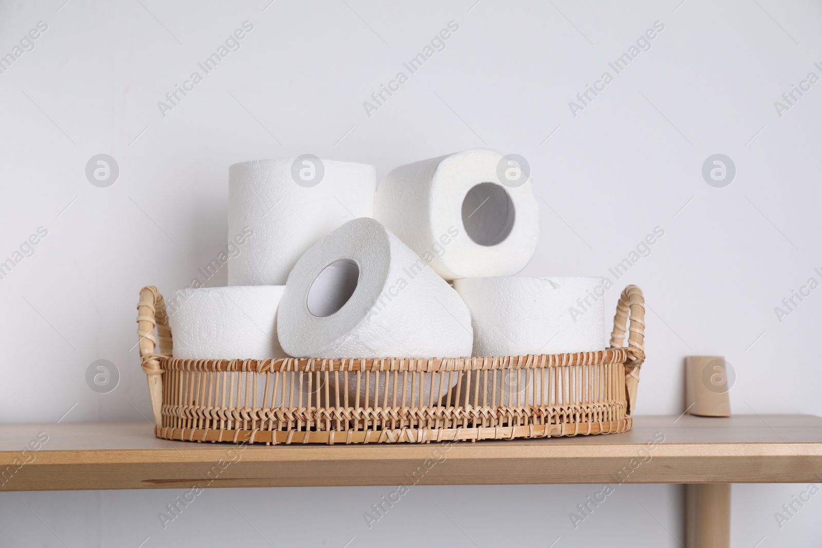 Photo of Toilet paper rolls in wicker basket on wooden table near white wall