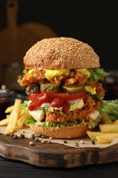 Delicious burger with crispy chicken patty and french fries on black wooden table, closeup