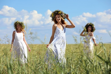 Young women wearing wreaths made of beautiful flowers in field on sunny day