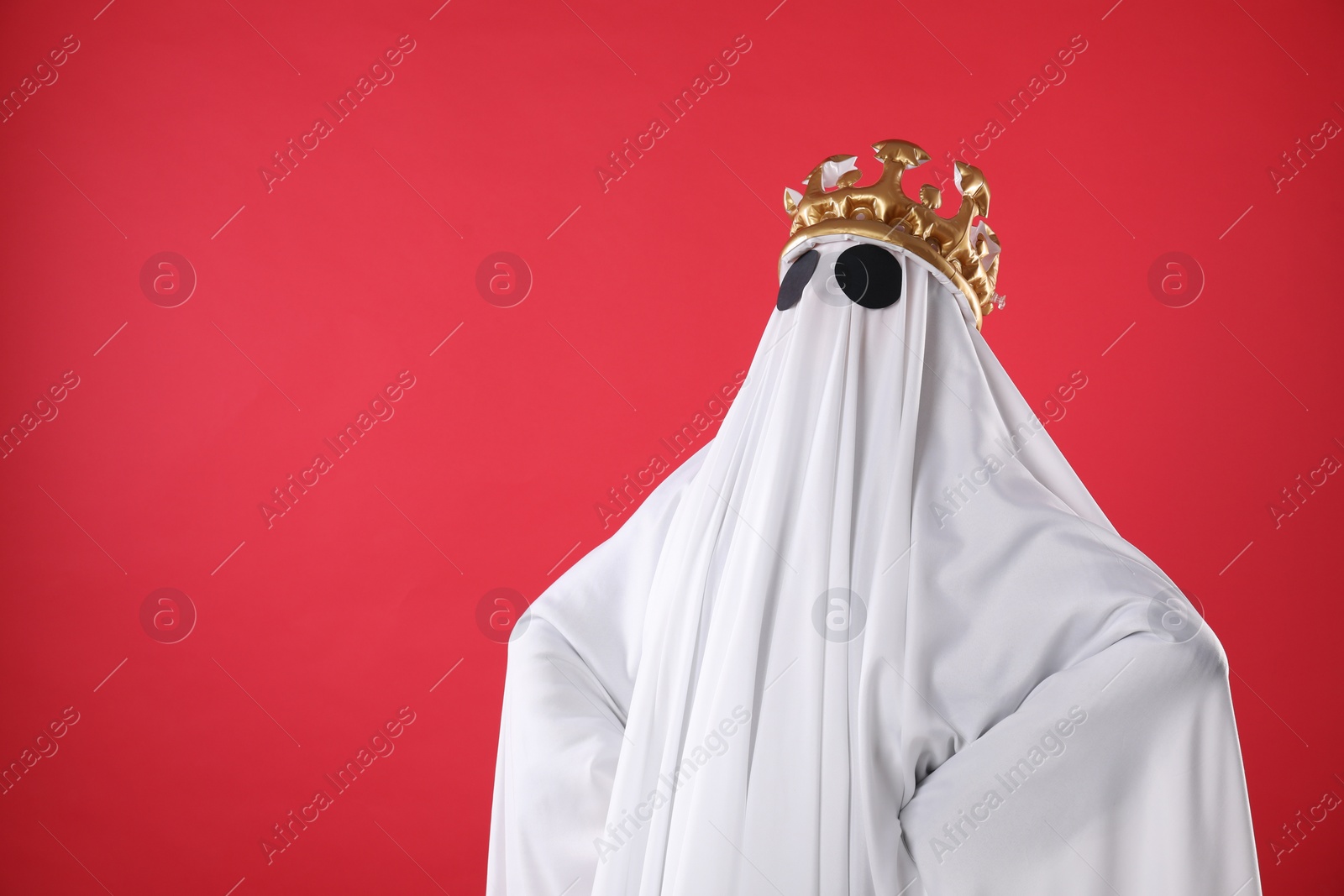 Photo of Person in ghost costume and luxurious crown on red background, space for text