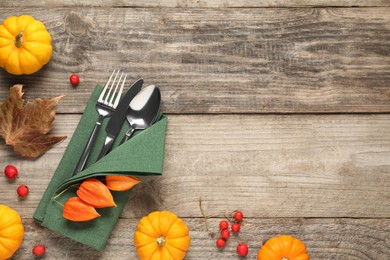 Photo of Cutlery, napkin and autumn decoration on wooden background, flat lay with space for text. Table setting