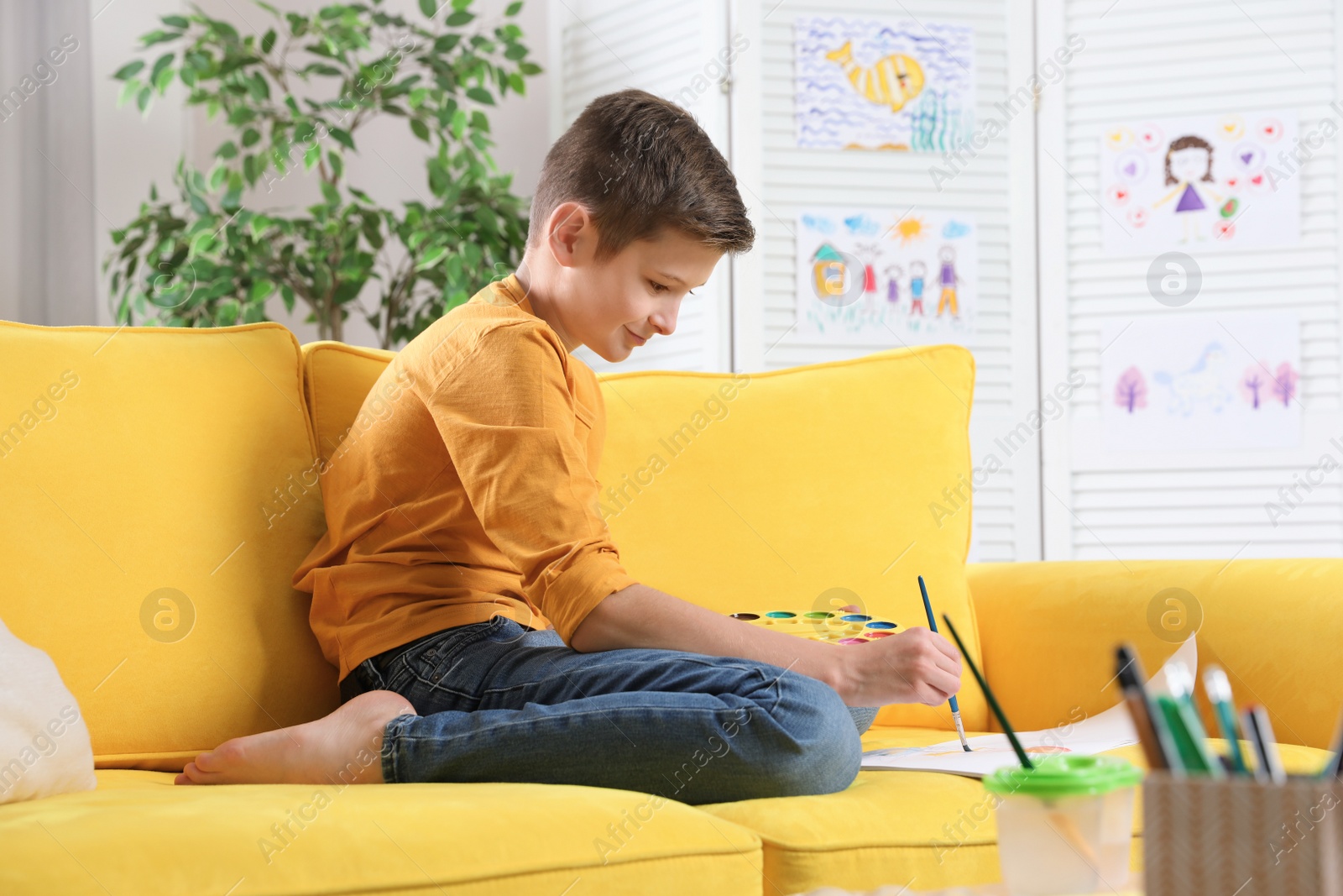 Photo of Little boy painting picture on sofa indoors