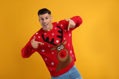 Photo of Emotional man pointing at his Christmas sweater on yellow background