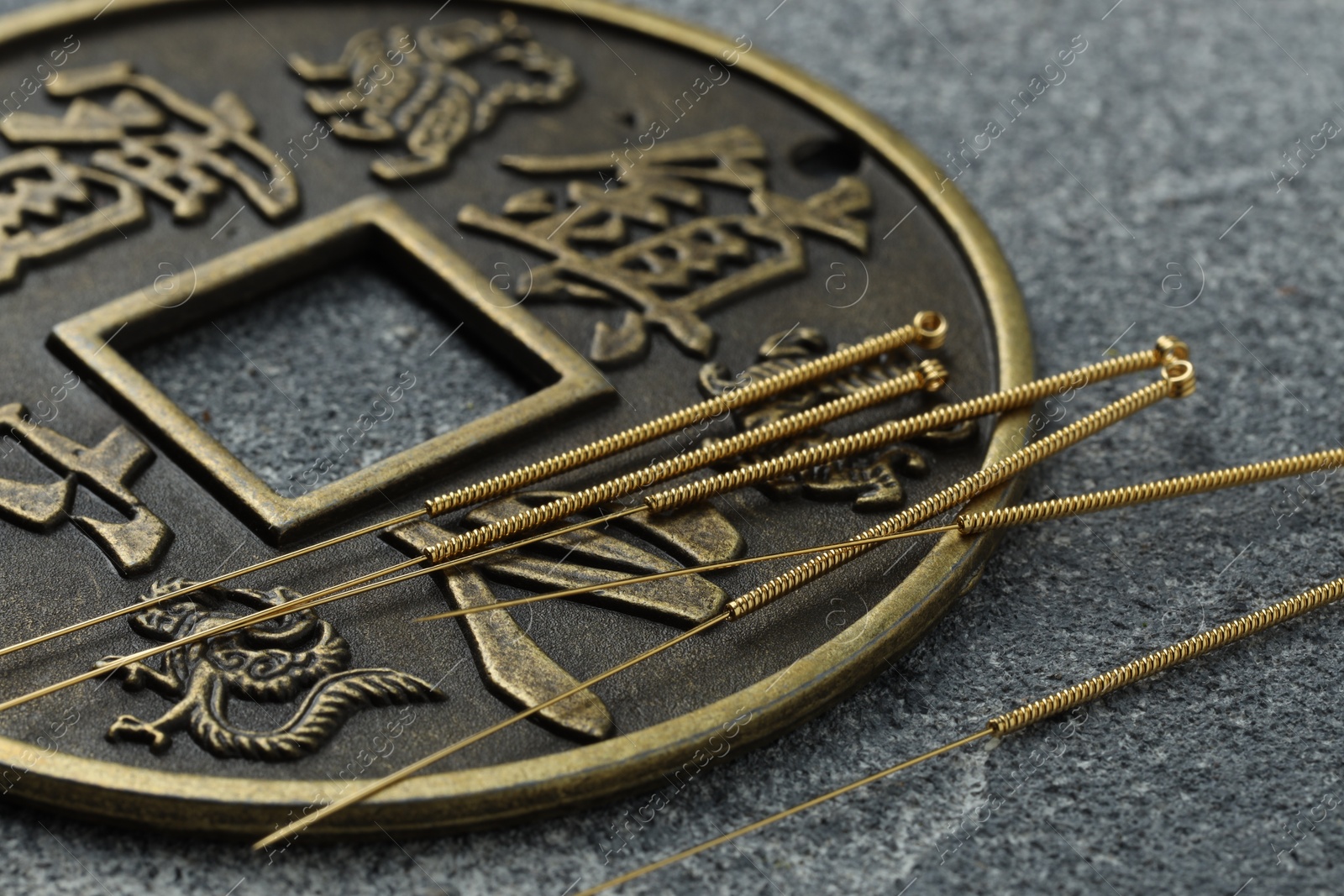 Photo of Acupuncture needles and Chinese coin on grey textured table, closeup