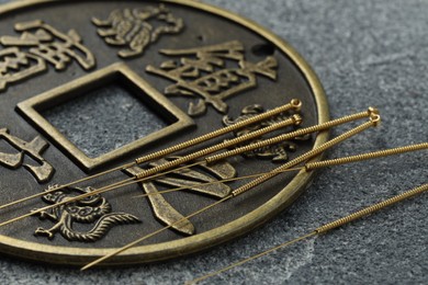 Acupuncture needles and Chinese coin on grey textured table, closeup