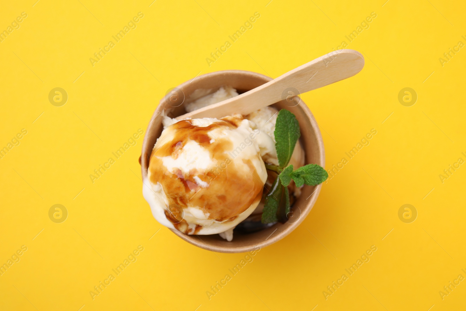 Photo of Scoops of ice cream with caramel sauce and mint leaves on yellow table, top view