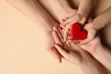 Parents and kid holding red heart in hands on beige background, top view