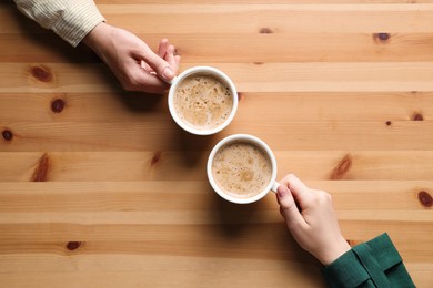 Women with cups of coffee at wooden table, top view