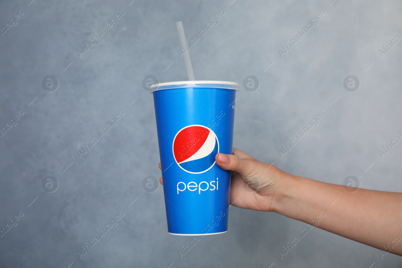 Photo of MYKOLAIV, UKRAINE - JUNE 9, 2021: Woman holding paper Pepsi cup on grey background, closeup