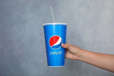 MYKOLAIV, UKRAINE - JUNE 9, 2021: Woman holding paper Pepsi cup on grey background, closeup