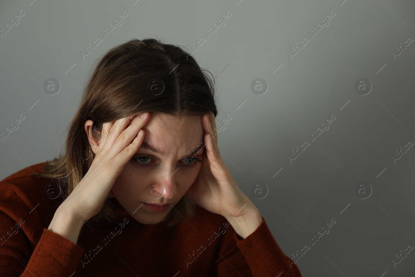 Photo of Sad young woman near grey wall indoors, space for text