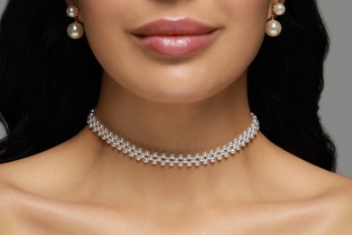 Young woman wearing elegant pearl jewelry on grey background, closeup