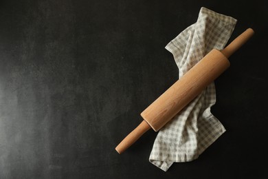 Rolling pin and kitchen towel on black table, top view. Space for text