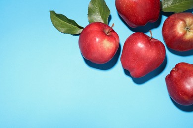 Photo of Ripe red apples and green leaves on light blue background, flat lay. Space for text