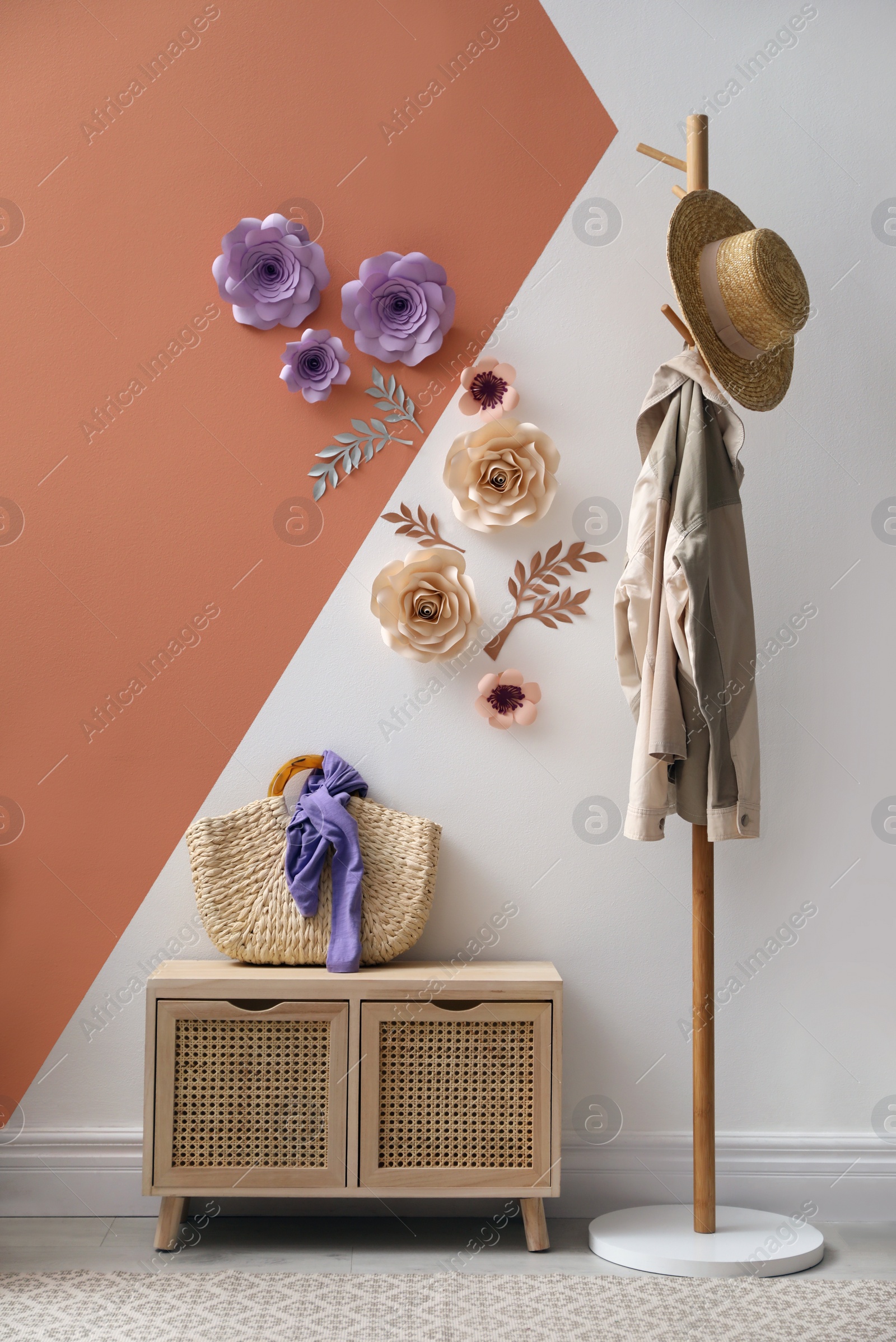 Photo of Cabinet and clothes rack near color wall with floral decor indoors