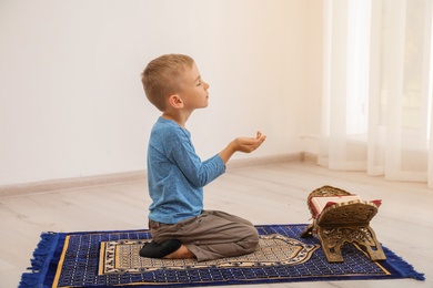 Photo of Little Muslim boy with Koran praying on rug indoors