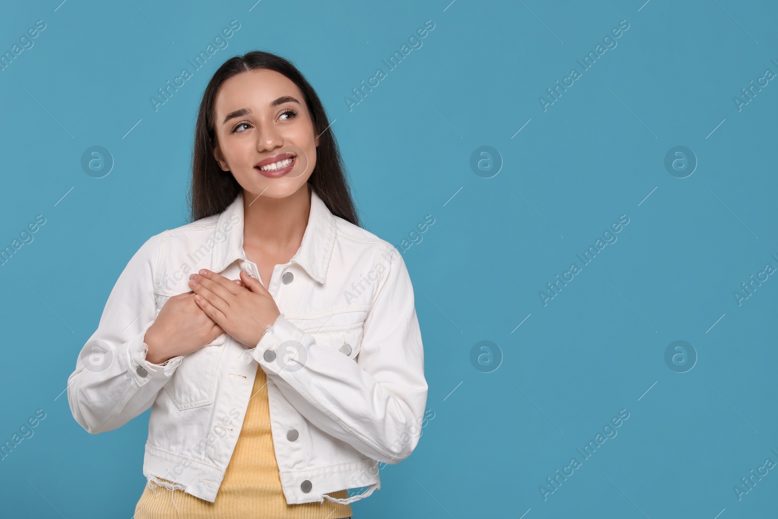 Photo of Thank you gesture. Beautiful grateful woman with hands on chest against light blue background, space for text