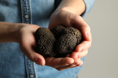 Woman holding heap of black truffles in hands on grey background, closeup