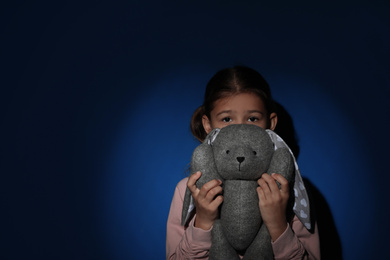 Photo of Sad little girl with toy near blue wall, space for text. Domestic violence concept