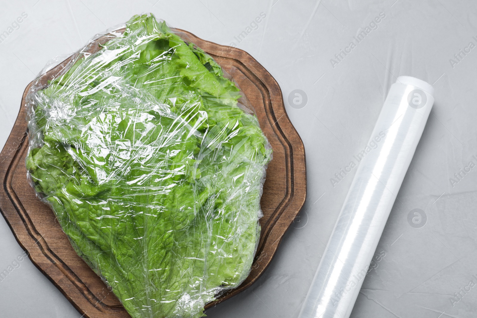 Photo of Fresh lettuce with plastic food wrap on light grey table, flat lay