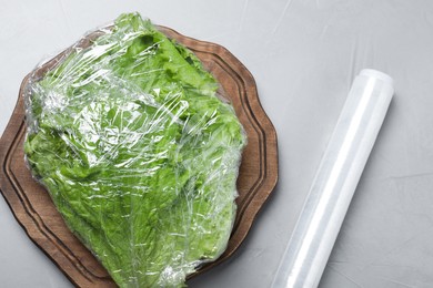 Fresh lettuce with plastic food wrap on light grey table, flat lay