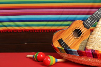 Mexican sombrero hat, ukulele and maracas on red table, closeup. Space for text