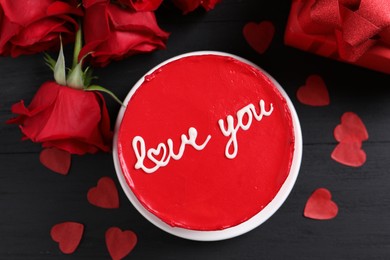 Photo of Bento cake with text Love You, roses, paper hearts and gift box on black wooden table, flat lay. St. Valentine's day surprise