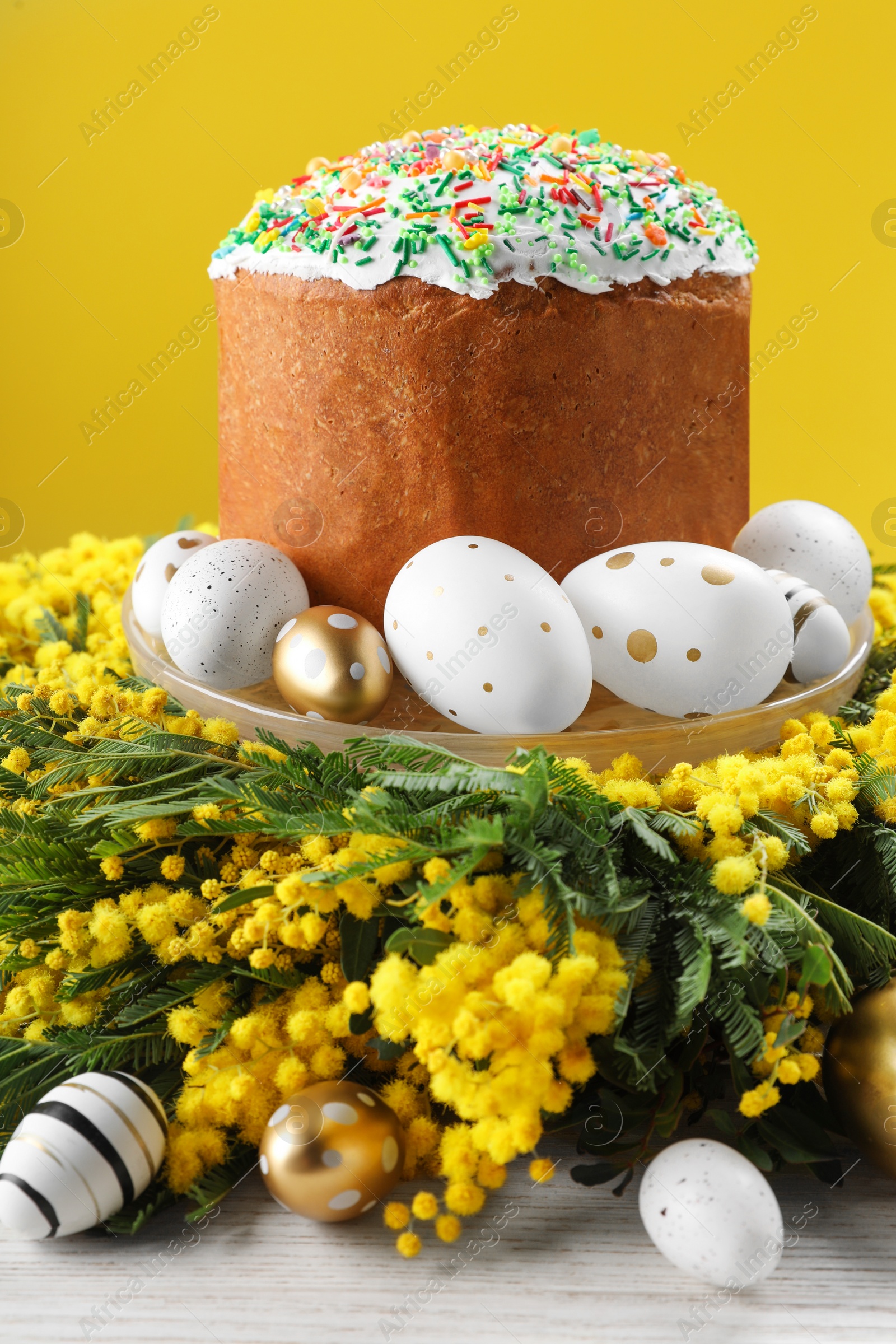 Photo of Traditional Easter cake with sprinkles, painted eggs and beautiful spring flowers on white wooden table