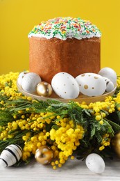 Traditional Easter cake with sprinkles, painted eggs and beautiful spring flowers on white wooden table