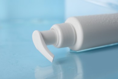 Photo of Wet bottle of face cleansing product on light blue background, closeup