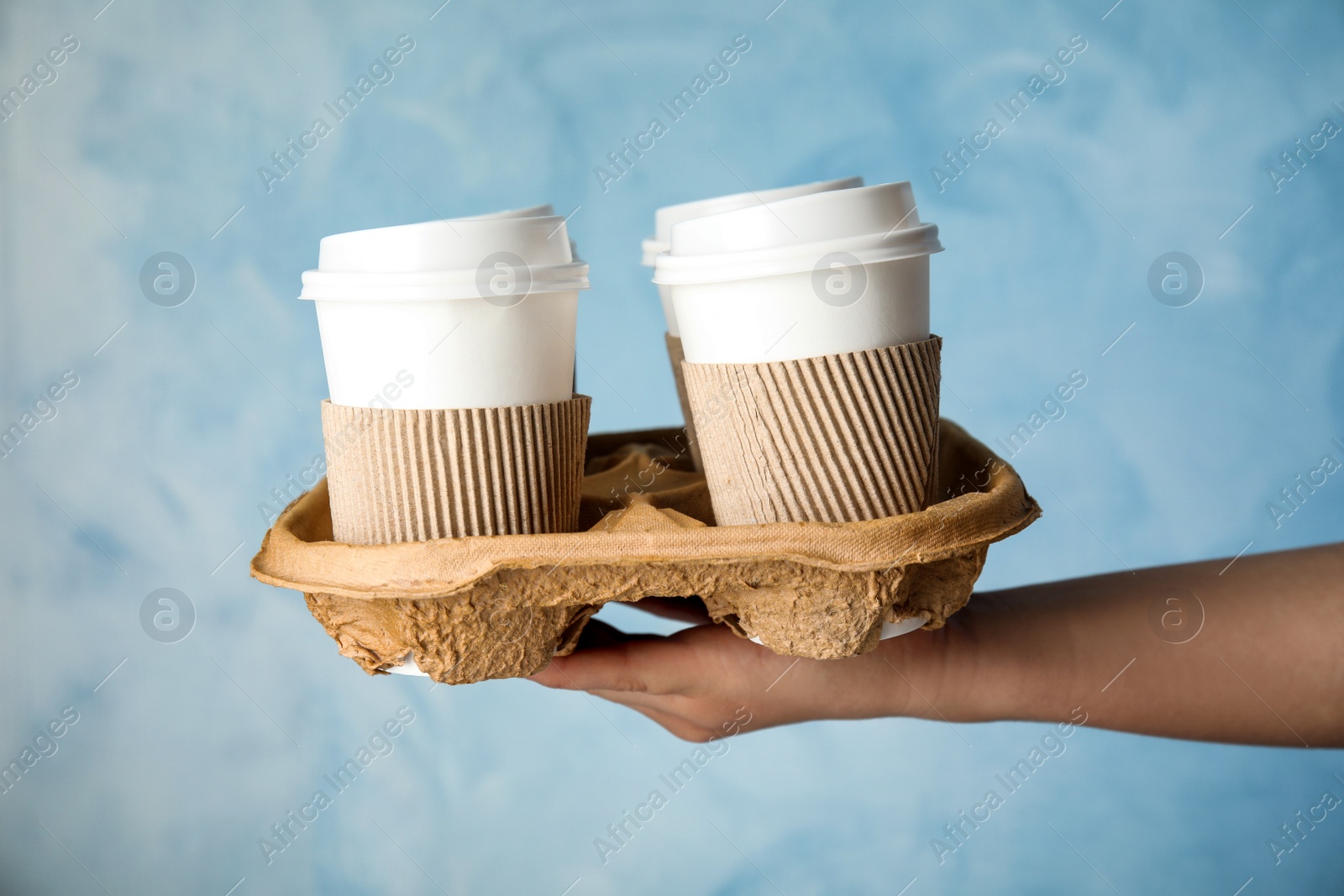 Photo of Woman holding cardboard holder with takeaway paper coffee cups on light blue background, closeup