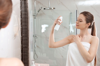 Young woman applying thermal water on face near mirror in bathroom. Cosmetic product