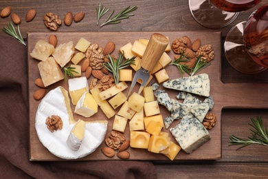 Photo of Cheese plate with rosemary and nuts on wooden table, flat lay