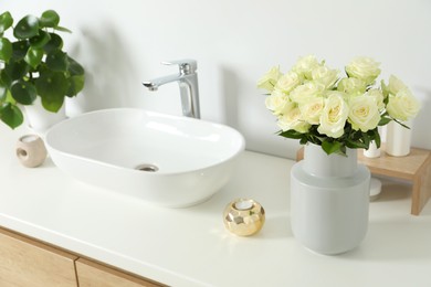 Vase with beautiful white roses and toiletries near sink in bathroom